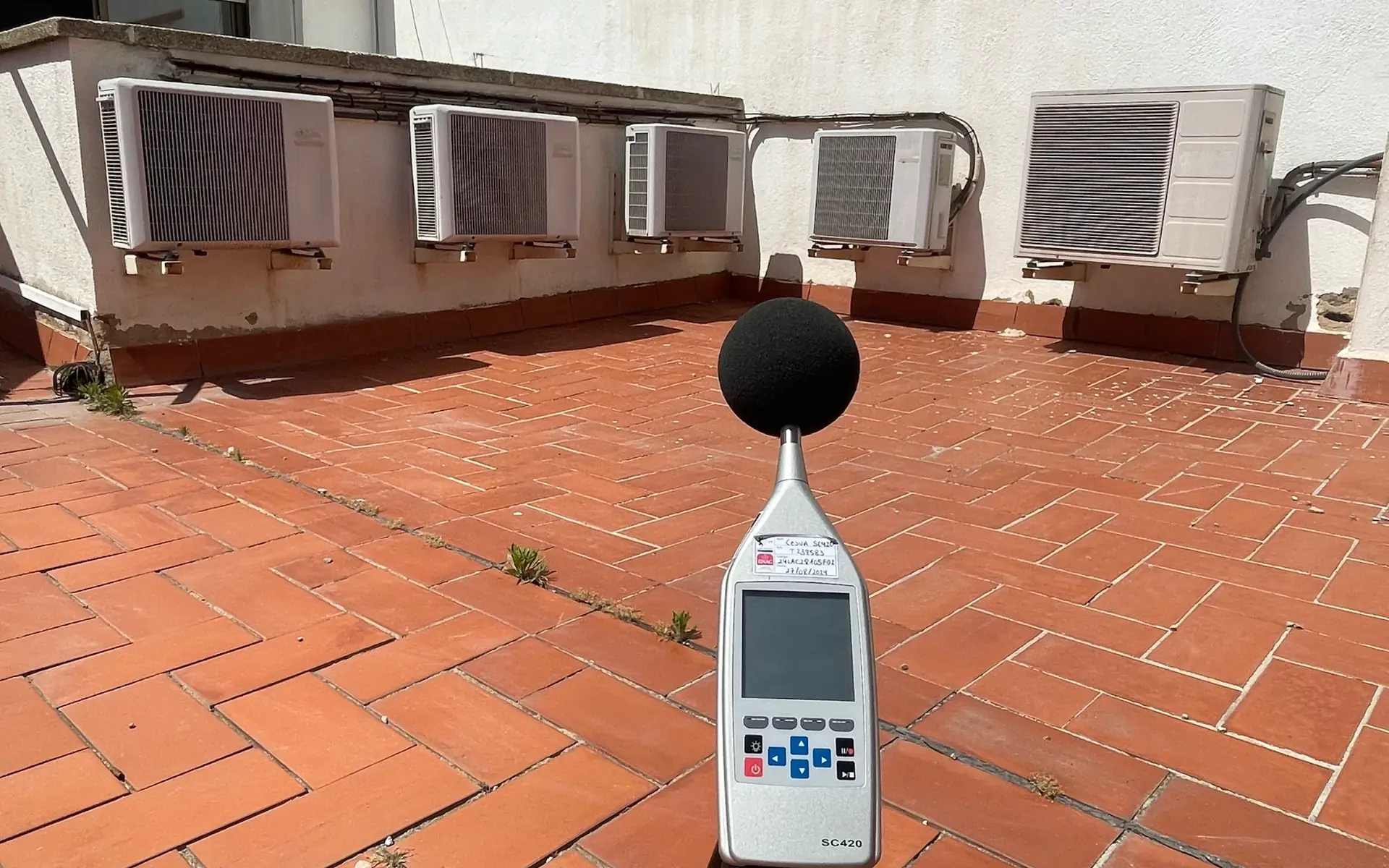 Sonòmetre sobre un trípode en un terrat mesurant el soroll d’unes instal·lacions de climatització